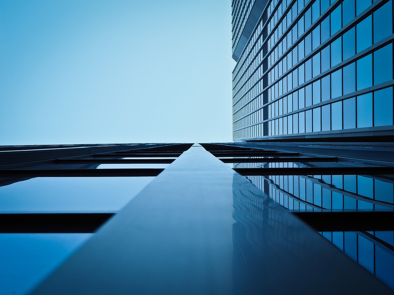 Modern glass skyscraper with blue reflective windows against a bright blue sky with white clouds